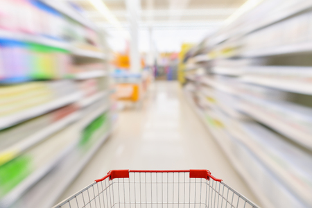 Empty shopping cart with abstract blur supermarket discount store aisle and product shelves interior defocused backgroundの写真素材