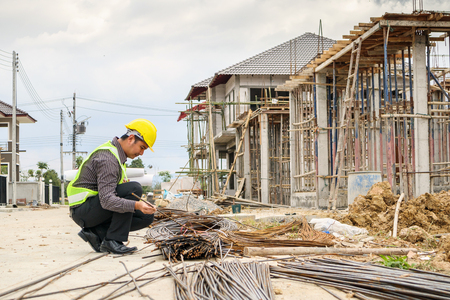 Asian business man construction engineer worker in protective helmet and blueprints paper on hand looking at steel bar at house building siteの写真素材