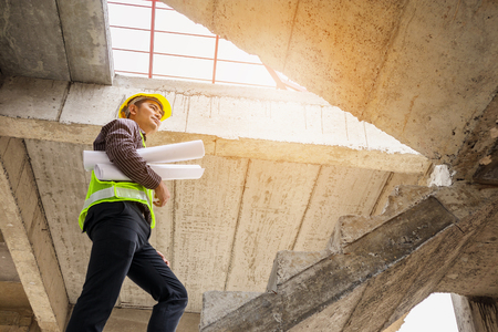 young professional engineer worker in protective helmet and blueprints paper on hand at the house building construction siteの写真素材