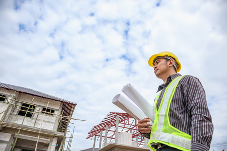 Asian business man construction engineer worker in protective helmet and blueprints paper on hand at house building siteの写真素材