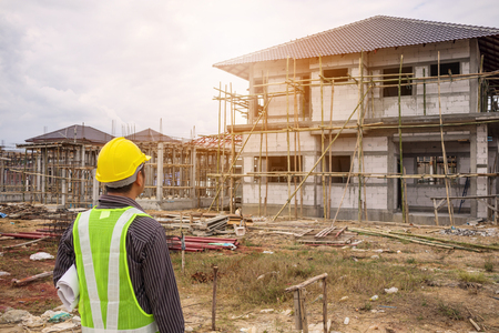 Asian business man construction engineer worker in protective helmet and blueprints paper on hand at house building siteの写真素材