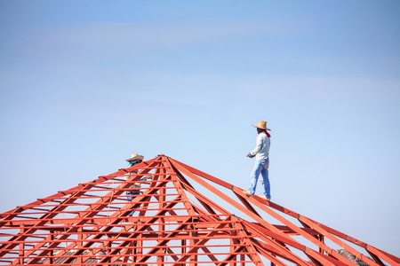Construction welder workers installing steel frame structure of the house roof at building construction site with clouds and skyの写真素材