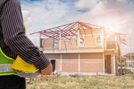 Asian business man construction engineer worker in protective helmet and blueprints paper on hand at house building siteの写真素材
