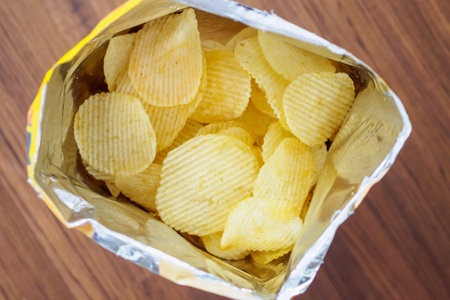 Potato chips in open snack bag close up on table floorの写真素材