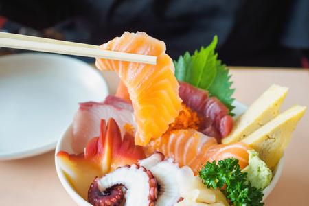 Salmon slice in chopsticks, Eating Sashimi Rice Bowl Chirashi Don Japanese foodの写真素材