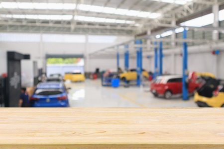 empty wood table over car service centre with auto at repair station bokeh light defocused blur backgroundの写真素材