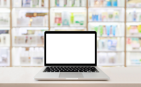 Laptop computer blank screen on pharmacy counter drugstore shop interior with medicines vitamins supplement and healthcare product on shelves blur backgroundの写真素材