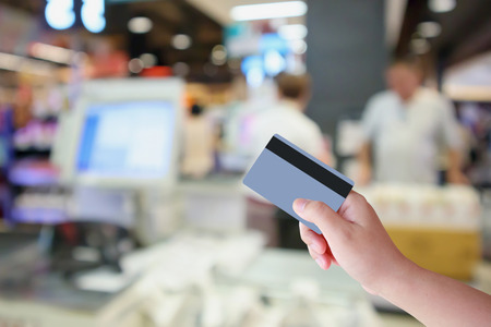 Hand hold credit card with Supermarket cashier checkout counter with customer defocused blur background, shopping and paying conceptの写真素材