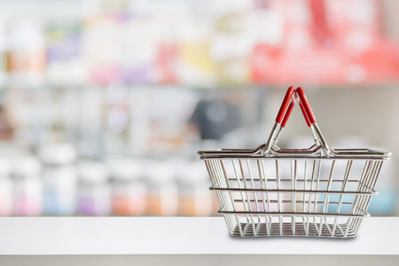 Empty shopping basket on pharmacy drugstore counter with blur shelves of medicine and vitamin supplements backgroundの写真素材