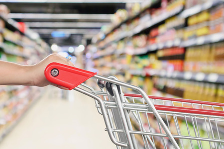 Woman hold shopping cart with abstract blur supermarket discount store aisle and product shelves interior defocused bokeh backgroundの写真素材