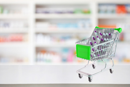 medicine pills blister pack capsule in shopping cart on pharmacy store counter with blur drugstore shelves defocused backgroundの写真素材