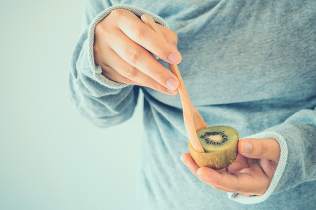 Young female eating ripe kiwi fruit with wooden spoonの写真素材
