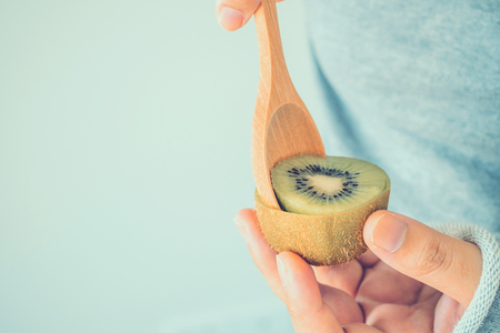 Young female eating ripe kiwi fruit with wooden spoonの写真素材