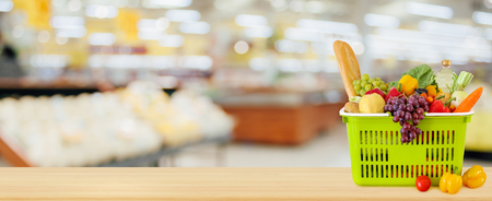 Shopping basket filled with fruits and vegetables on wood table with supermarket grocery store blurred defocused background with bokeh lightの写真素材