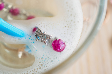 cleaning vintage jewelry diamond ring and bracelet with glass of hot water and dishwashing liquid on wood table backgroundの写真素材