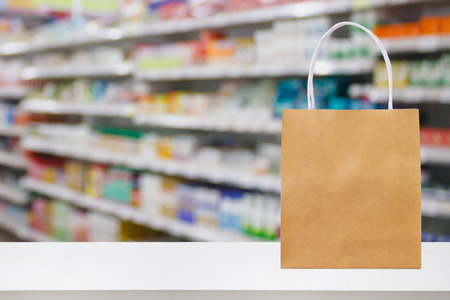 Paper bag on Pharmacy drugstore counter table with medicine and healthcare product on shelves blur backgroundの写真素材