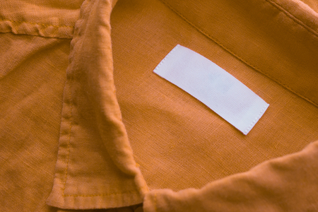 White blank clothing tag label on brown linen shirt fabric texture backgroundの写真素材