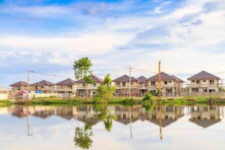 New house building reflection with water in lake at residential estate construction site with clouds and blue skyの写真素材