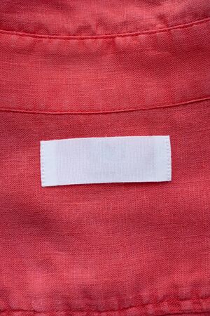 White blank clothing tag label on red linen shirt fabric texture background