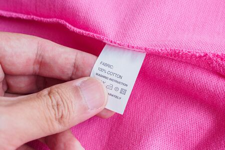 Woman reading on laundry care washing instructions clothes label on pink cotton shirtの写真素材