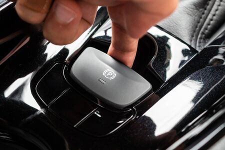 Hand push on electronic handbrake button in luxury modern car