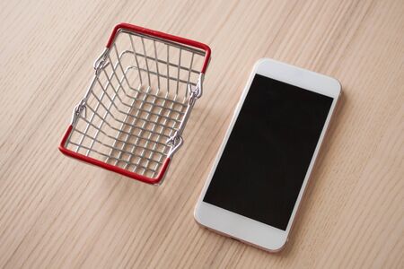 Mobile phone with basket on wood table background shopping online conceptの写真素材