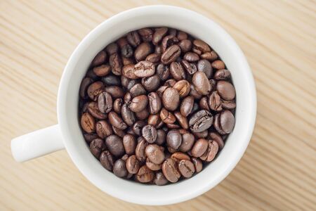 fresh roasted coffee beans in white cup on wood table, top viewの写真素材