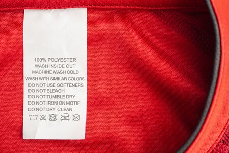 White laundry care washing instructions clothes label on red jersey polyester sport shirtの写真素材