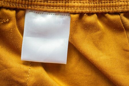 White blank clothing tag label on brown cotton shorts fabric texture background