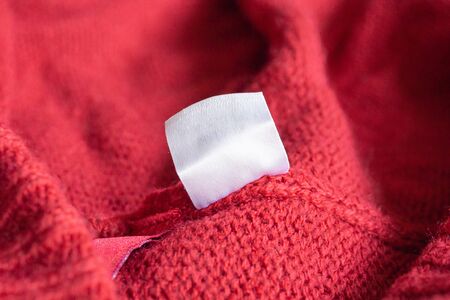 Blank white laundry care clothing label on red knitted texture background