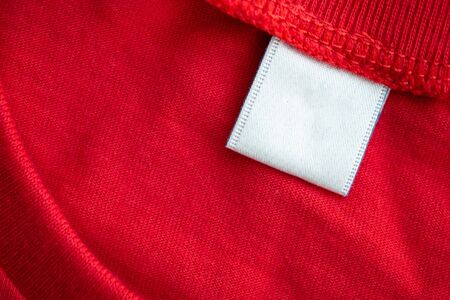 White blank clothing tag label on new red cotton shirt fabric texture backgroundの写真素材
