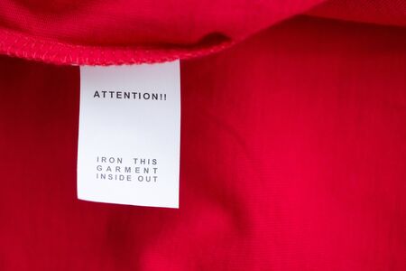 White laundry care washing instructions clothes label on red cotton shirt