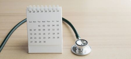 Stethoscope with calendar page date on wood table background doctor appointment medical conceptの写真素材