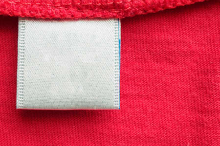 White blank laundry care clothes label on red cotton shirt background