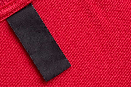 Blank black laundry care clothes label on red fabric texture background