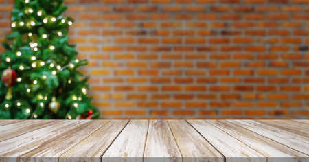 Empty wood table top with blur decorated Christmas tree with baubles on brick wall background