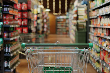 empty green shopping cart in supermarket aisle interior backgroundの写真素材