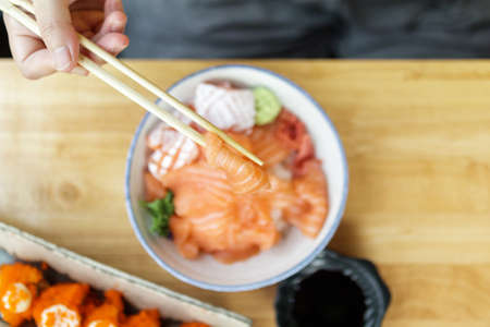 Asian woman eating salmon slice sashimi with rice in Japanese restaurant