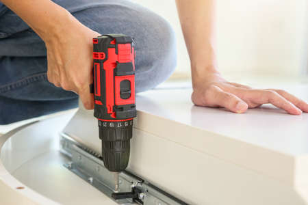 man assembling white table furniture at home using cordless screwdriverの写真素材