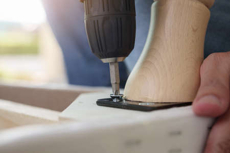 Man assembling sofa furniture at home using cordless screwdriver