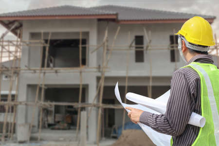 young professional engineer in protective helmet and blueprints paper at the house building...