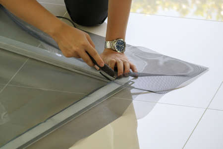 man install mosquito net wire screen on house window protection against insectの写真素材