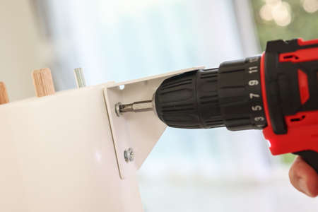 man assembling white table furniture at home using cordless screwdriverの写真素材