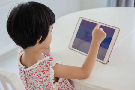 Little asian girl playing digital tablet at homeの写真素材