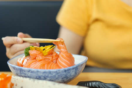 Asian woman eating salmon slice sashimi with rice in Japanese restaurantの写真素材