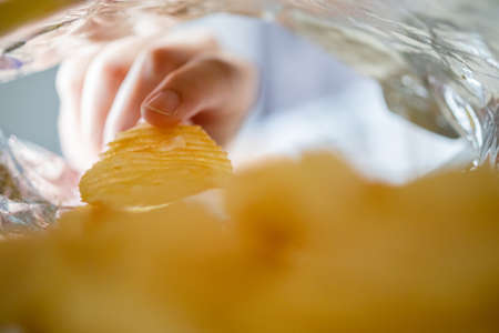 Hand picking potato chips inside snack bag