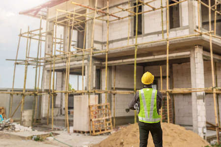 young professional engineer in protective helmet and blueprints paper at the house building construction siteの写真素材
