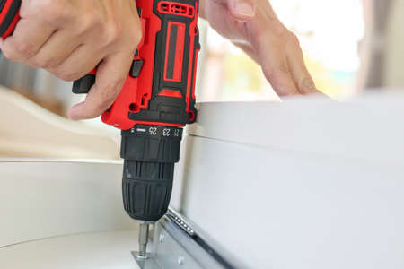 man assembling white table furniture at home using cordless screwdriver