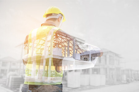 Double exposure image of professional engineer in protective helmet and blueprints paper at the...