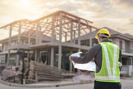 young professional engineer in protective helmet and blueprints paper at the house building...